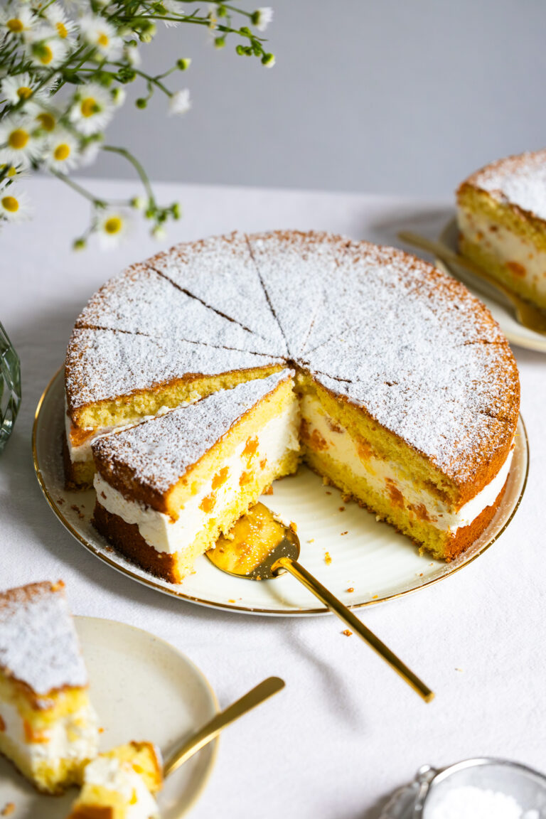 käsesahnetorte von schräg vorne fotografiert, in stücke geschnitten, ein stück ist auf einem tortenheber.